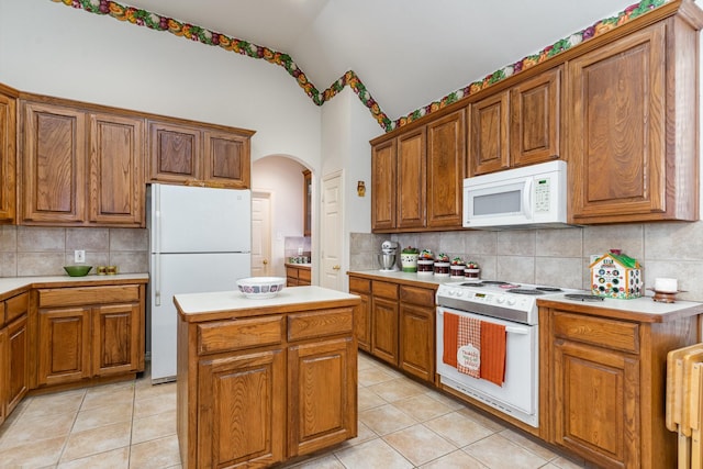 kitchen featuring lofted ceiling, a center island, light tile patterned floors, and white appliances