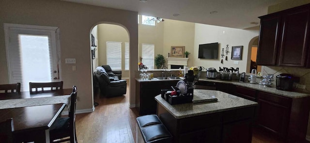 kitchen with light wood-type flooring, a kitchen island, a breakfast bar, and light stone countertops