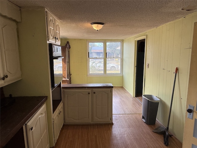 kitchen with double oven, wooden walls, kitchen peninsula, a textured ceiling, and light hardwood / wood-style floors