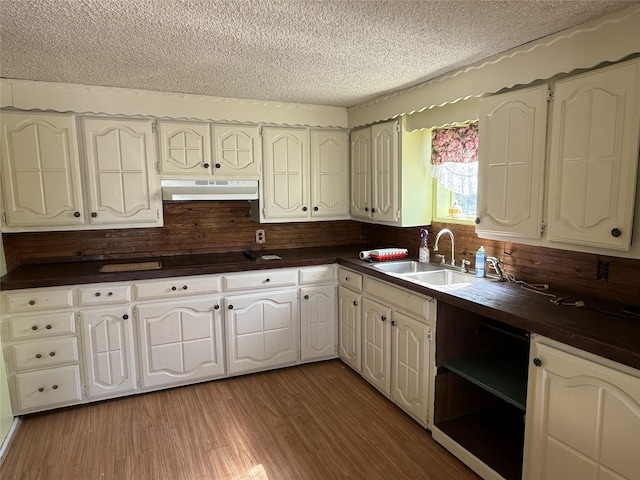 kitchen with hardwood / wood-style floors, white cabinets, wood counters, a textured ceiling, and sink