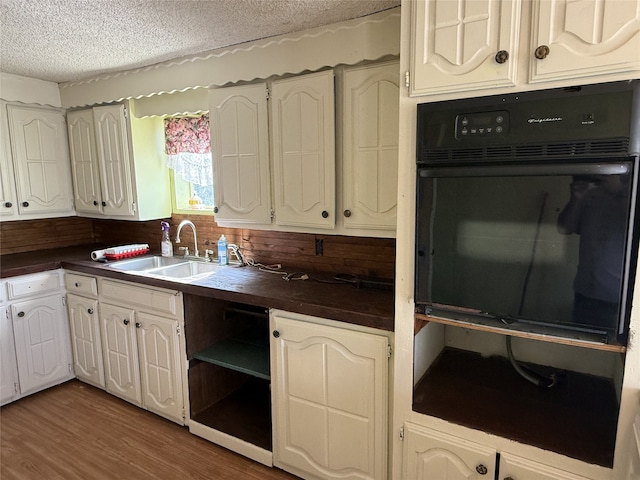 kitchen featuring oven, sink, white cabinetry, a textured ceiling, and dark hardwood / wood-style flooring