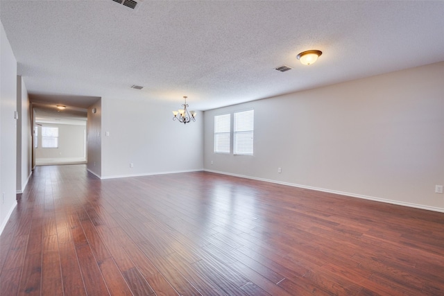 unfurnished room featuring dark hardwood / wood-style floors, a textured ceiling, and an inviting chandelier