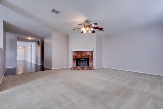 unfurnished living room featuring ceiling fan, a brick fireplace, light colored carpet, and a textured ceiling