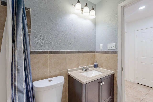 bathroom with toilet, vanity, tile walls, and tile patterned flooring