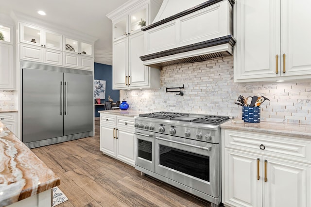 kitchen featuring white cabinets, backsplash, light stone countertops, light hardwood / wood-style floors, and premium appliances