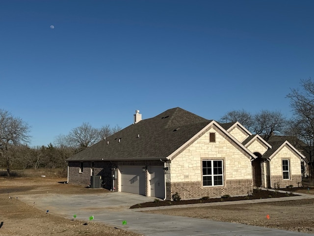 view of front facade featuring cooling unit, roof with shingles, concrete driveway, an attached garage, and a chimney