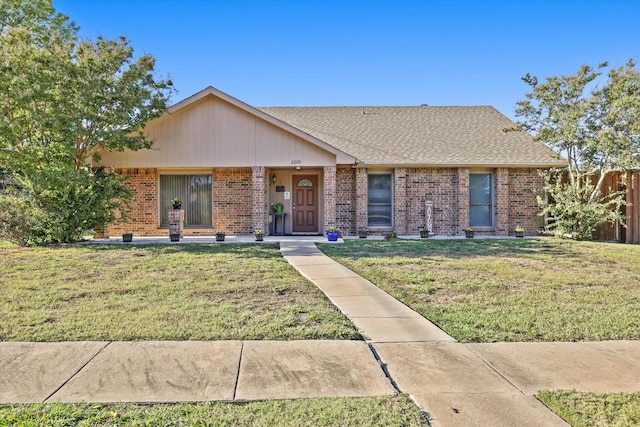 view of front of house featuring a shingled roof, a front lawn, and brick siding