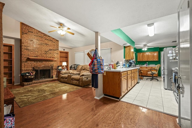 kitchen with ceiling fan, light hardwood / wood-style floors, vaulted ceiling, a fireplace, and appliances with stainless steel finishes