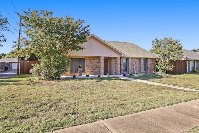 ranch-style house featuring brick siding, roof with shingles, fence, and a front yard