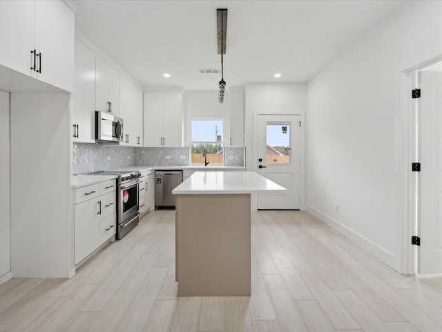 kitchen with stainless steel appliances, pendant lighting, white cabinets, light hardwood / wood-style floors, and a kitchen island