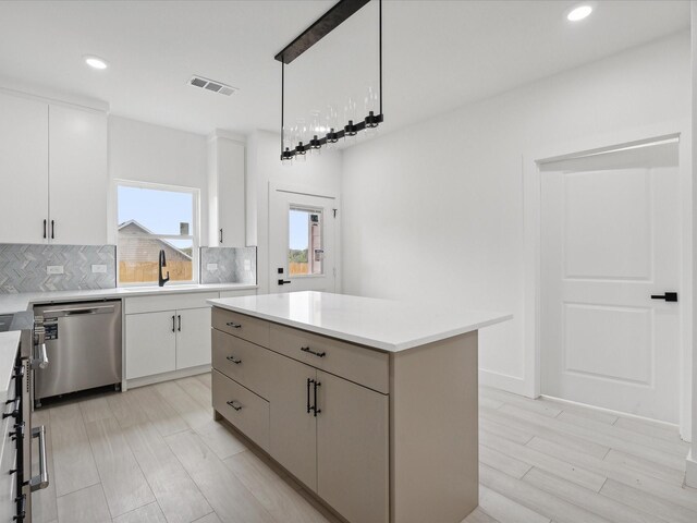 kitchen with stainless steel dishwasher, decorative backsplash, a center island, and white cabinetry