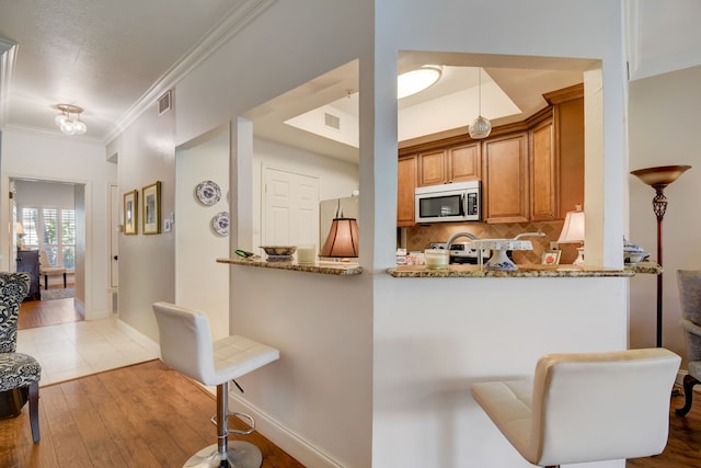 kitchen with kitchen peninsula, appliances with stainless steel finishes, light hardwood / wood-style floors, and light stone countertops