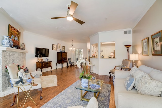 living room with a brick fireplace, hardwood / wood-style floors, ceiling fan with notable chandelier, and crown molding