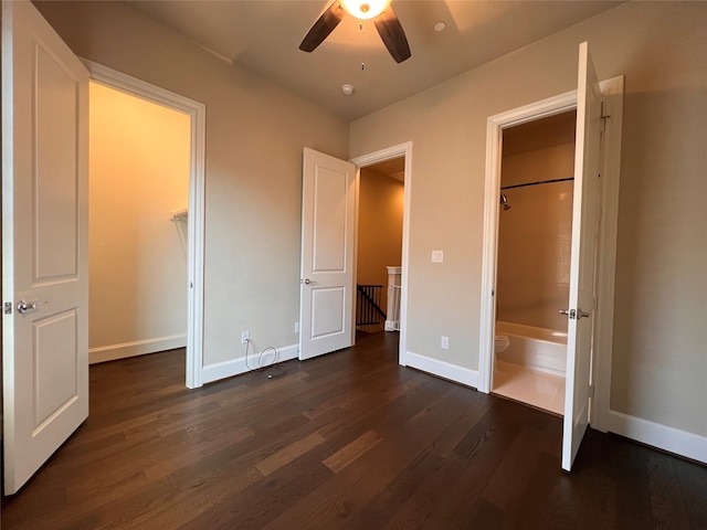 unfurnished bedroom with ensuite bath, dark wood-type flooring, a walk in closet, and ceiling fan