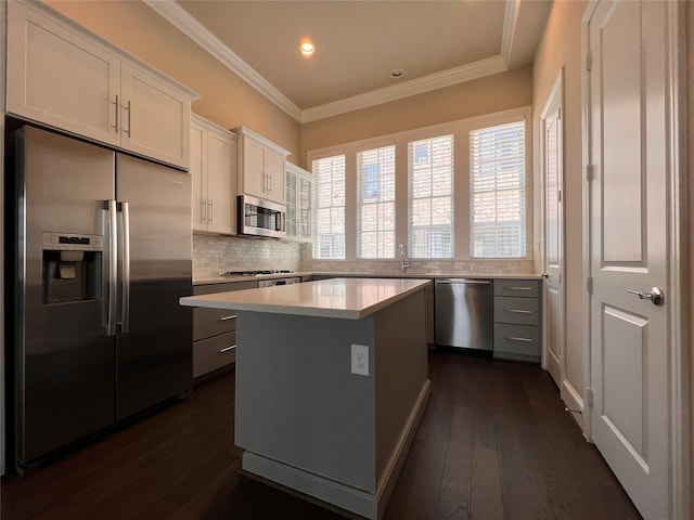 kitchen featuring dark wood-type flooring, stainless steel appliances, ornamental molding, a center island, and white cabinetry