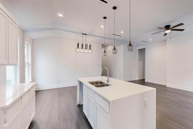 kitchen featuring decorative light fixtures, light countertops, a kitchen island with sink, a sink, and white cabinetry