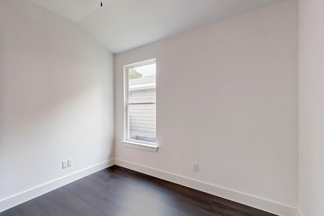 spare room featuring vaulted ceiling, dark wood-style flooring, and baseboards