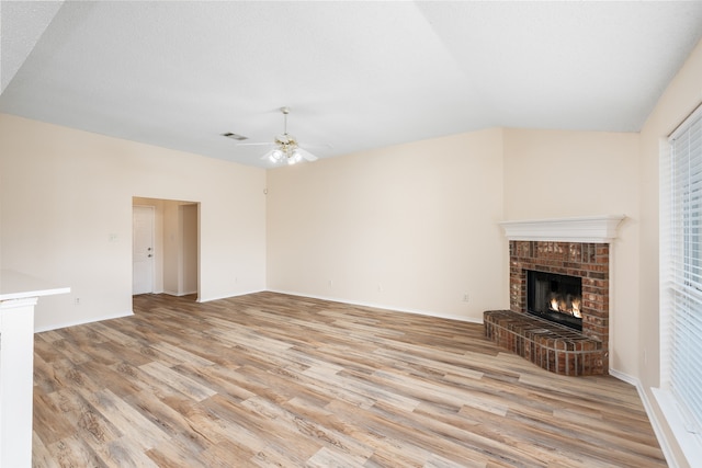 unfurnished living room featuring a textured ceiling, a brick fireplace, light hardwood / wood-style floors, ceiling fan, and lofted ceiling