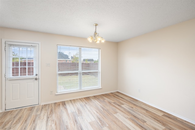 unfurnished dining area featuring light hardwood / wood-style floors, a notable chandelier, and a textured ceiling