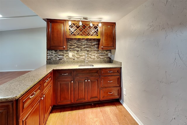 bar with sink, light stone countertops, light wood-type flooring, and tasteful backsplash