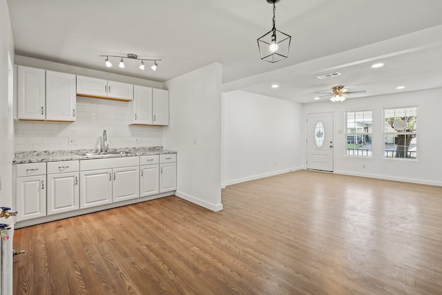 kitchen featuring sink, light wood-type flooring, pendant lighting, white cabinets, and decorative backsplash