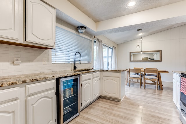 kitchen featuring lofted ceiling, white cabinets, tasteful backsplash, beverage cooler, and sink