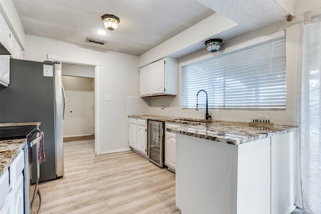 kitchen with sink, light wood-type flooring, stainless steel range with electric cooktop, white cabinetry, and beverage cooler