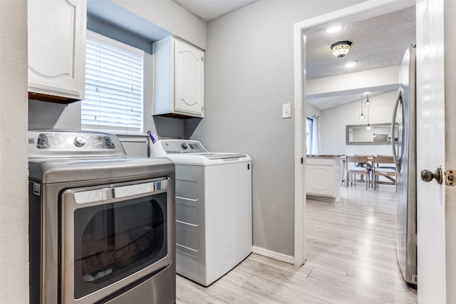 laundry area with cabinets, a textured ceiling, separate washer and dryer, and light wood-type flooring