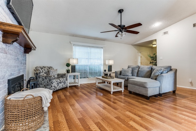 living room with a textured ceiling, a brick fireplace, ceiling fan, vaulted ceiling, and hardwood / wood-style flooring