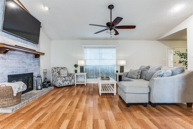 living room with hardwood / wood-style floors, vaulted ceiling, a brick fireplace, and a textured ceiling