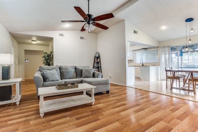 living room with a brick fireplace, a textured ceiling, light wood-type flooring, and ceiling fan