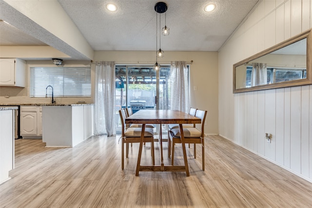 dining room with wood walls, a textured ceiling, lofted ceiling, and light wood-type flooring