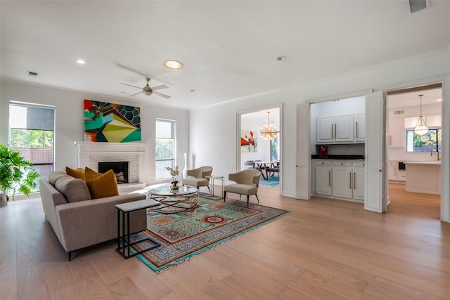 living room with a brick fireplace, light hardwood / wood-style floors, a healthy amount of sunlight, and ceiling fan