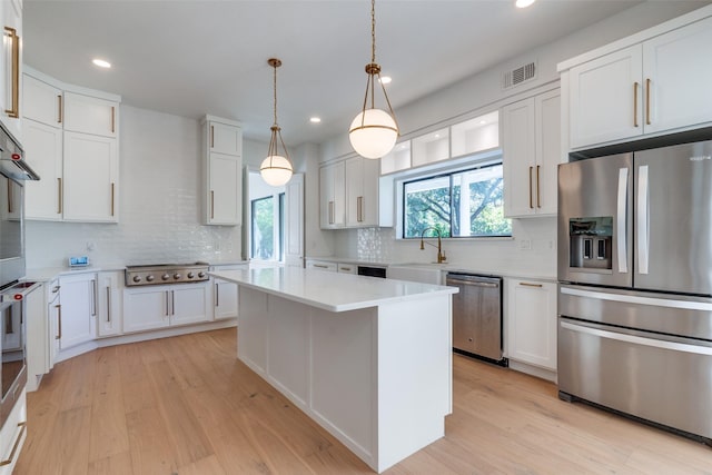 kitchen with a center island, backsplash, white cabinets, light hardwood / wood-style flooring, and stainless steel appliances