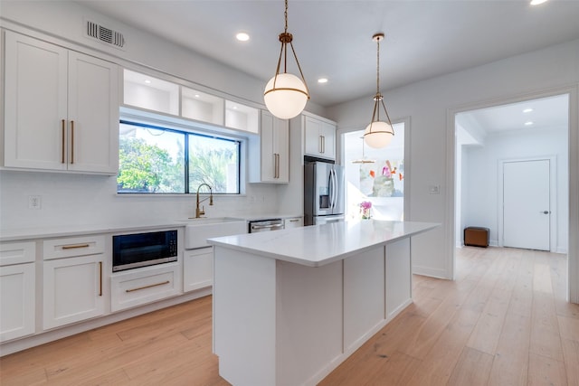 kitchen with white cabinets, appliances with stainless steel finishes, decorative light fixtures, a kitchen island, and light wood-type flooring