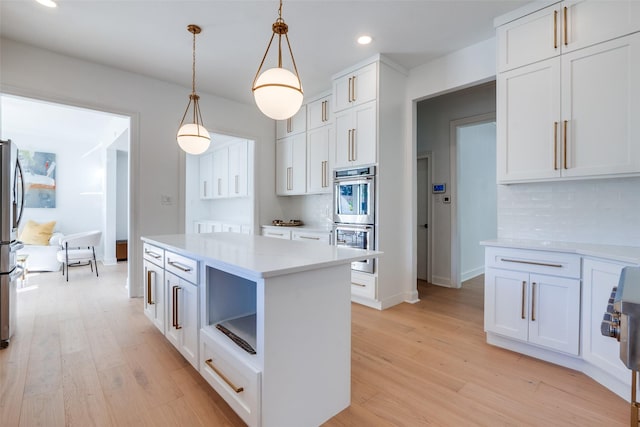 kitchen with light wood-type flooring, white cabinetry, hanging light fixtures, and appliances with stainless steel finishes