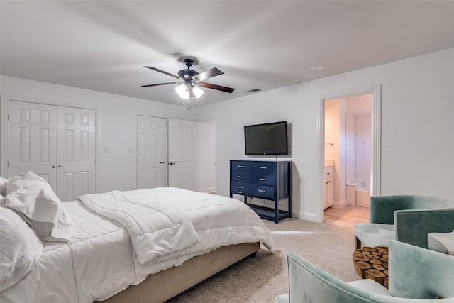 bedroom featuring ensuite bathroom, ceiling fan, light carpet, and two closets