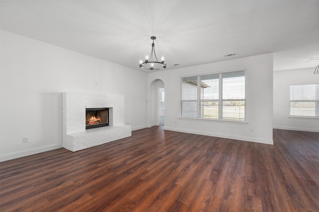 unfurnished living room with a brick fireplace, a chandelier, and dark hardwood / wood-style floors