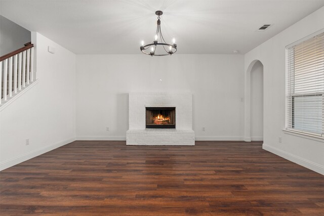 unfurnished living room with a brick fireplace, dark wood-type flooring, and a chandelier