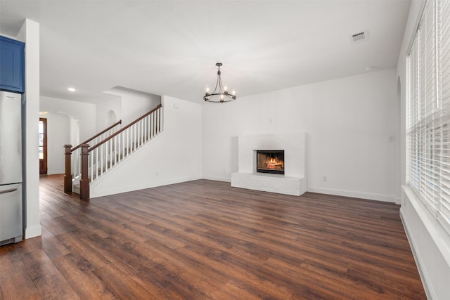 unfurnished living room with dark wood-type flooring, a notable chandelier, and a fireplace