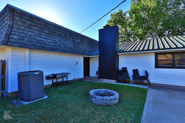 rear view of house featuring central AC, an outdoor fire pit, and a lawn