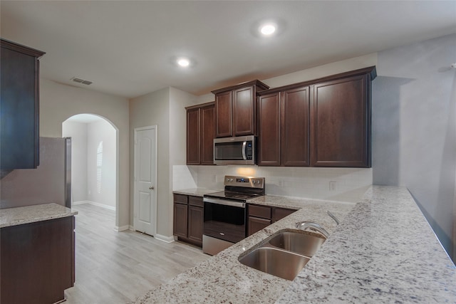 kitchen with stainless steel appliances, light stone counters, sink, tasteful backsplash, and dark brown cabinets