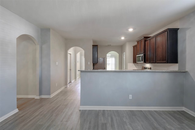 kitchen featuring dark brown cabinetry, kitchen peninsula, light stone counters, appliances with stainless steel finishes, and light hardwood / wood-style flooring