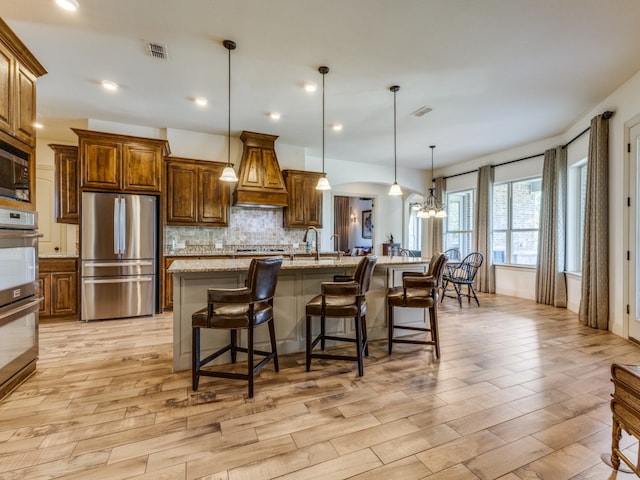 kitchen with a breakfast bar area, appliances with stainless steel finishes, a spacious island, pendant lighting, and light stone counters