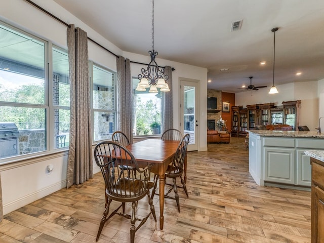 dining room featuring a fireplace, ceiling fan with notable chandelier, and light wood-type flooring