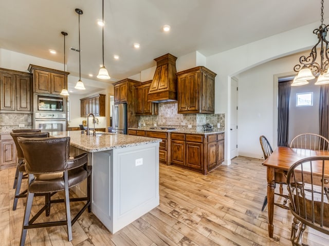 kitchen featuring light hardwood / wood-style flooring, appliances with stainless steel finishes, hanging light fixtures, and a kitchen island with sink