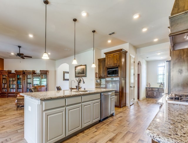 kitchen with hanging light fixtures, appliances with stainless steel finishes, a kitchen island with sink, light hardwood / wood-style flooring, and sink