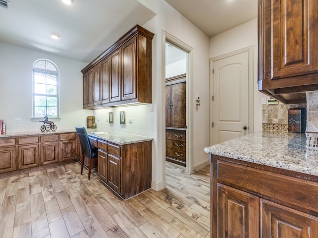 kitchen with built in desk, light stone counters, light wood-type flooring, and backsplash