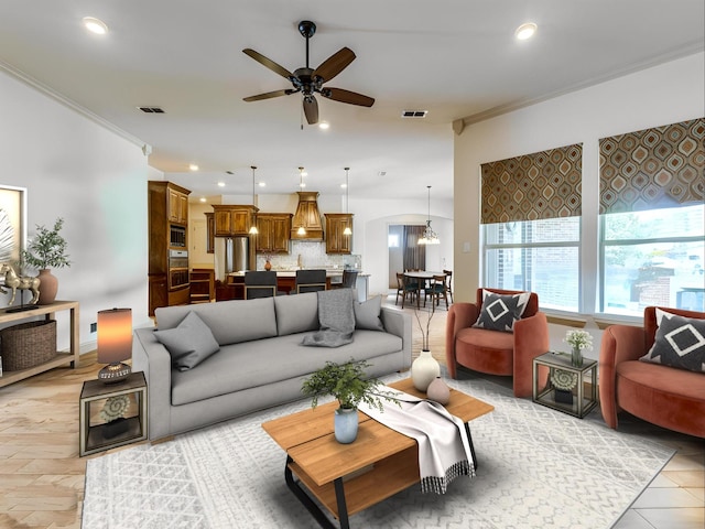 living room with ornamental molding, light wood-type flooring, and ceiling fan with notable chandelier