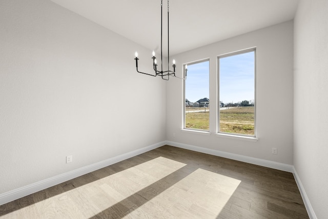 unfurnished dining area featuring dark wood-style flooring, baseboards, and an inviting chandelier